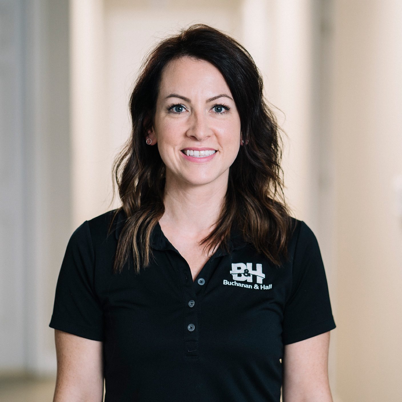 Headshot of a smiling female employee in a dark blue polo shirt, with a BH logo on the one side of her shirt