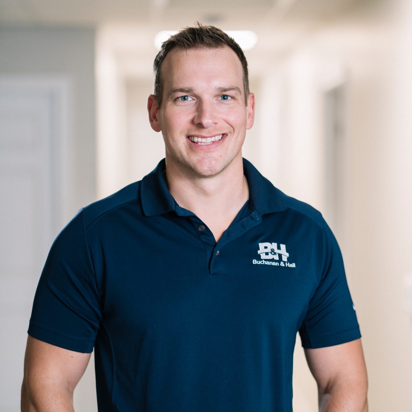 Headshot of a smiling male employee in a blue polo shirt, with a BH logo on the one side of his shirt